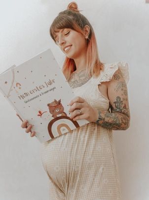 Schwangere Frau hält lächelnd das Eulentaler Babyalbum „Mein erstes Jahr – Glücksmomente & Erinnerungen“ mit Eulen- und Regenbogenmotiv vor ihren Babybauch.
