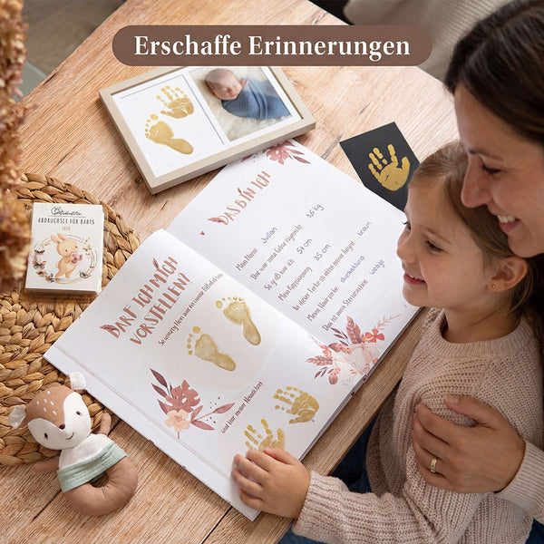 Mutter und Kind betrachten ein geöffnetes Eulentaler Babyalbum mit goldenen Hand- und Fußabdrücken, Geburtsdaten und gerahmtem Babyfoto.
