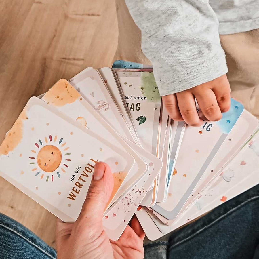 Erwachsener und Kind halten gemeinsam Eulentaler Affirmationskarten mit positiven Botschaften wie „Ich bin wertvoll“.
