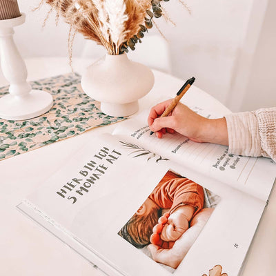 Hand schreibt in ein Babytagebuch - ein Babybild ist eingeklebt.