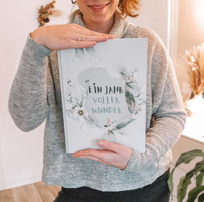 Frau hält stolz ein Babytagebuch "Ein Jahr voller Wunder" in den Händen.