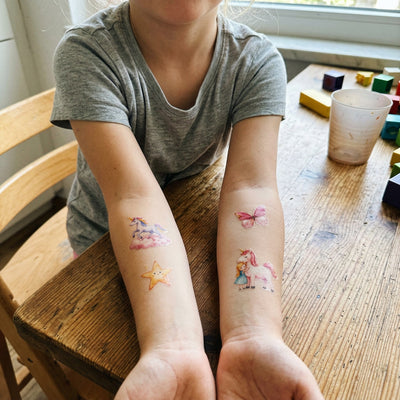 Kind zeigt Eulentaler Kindertattoos mit Einhörnern, Schmetterling und Stern auf beiden Unterarmen