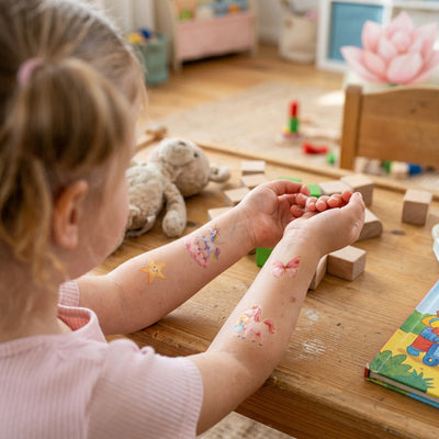 Kind zeigt mehrere Eulentaler Kindertattoos mit Einhörnern, Sternen und Regenbogen auf dem Arm