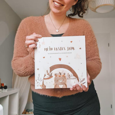 Frau hält lächelnd das Eulentaler Babyalbum „Mein erstes Jahr – Glücksmomente & Erinnerungen“ mit liebevoll illustriertem Boho-Cover in die Kamera.
