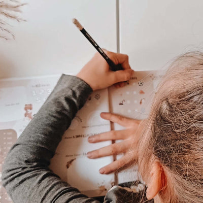 Kind füllt das geöffnete Eulentaler Kindergarten-Freundebuch im Boho-Design mit Waldtiermotiven und altersgerechten Fragen aus.
