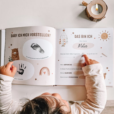 Kind betrachtet ein geöffnetes Eulentaler Babyalbum mit persönlichen Geburtsdaten sowie schwarzen Hand- und Fußabdrücken.
