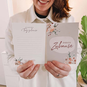 Frau hält eine Karte mit der Aufschrift "Endlich Zuhause" aus einem Erinnerungsset für den ersten Tag zu Hause.