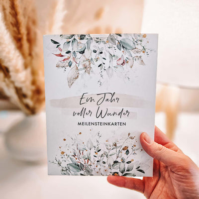 Hand hält das Set "Ein Jahr voller Wunder" mit floralen Mustern und goldenen Akzenten.