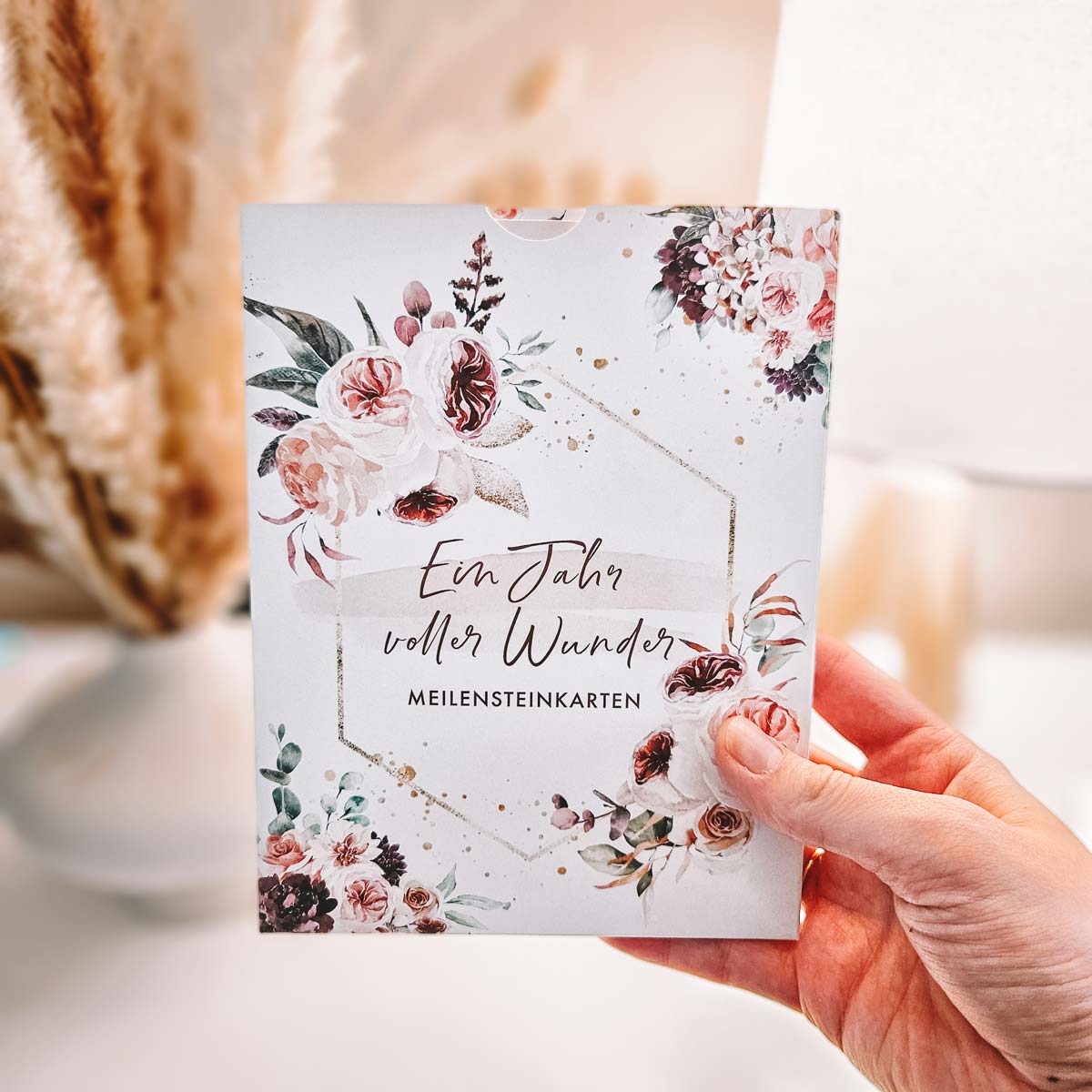 Hand hält das Set "Ein Jahr voller Wunder" mit floralen Mustern auf der Verpackung in die Kamera.