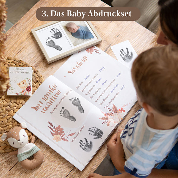 Eulentaler Baby-Abdruckset mit schwarzen Hand- und Fußabdrücken im geöffneten Babytagebuch sowie Bilderrahmen mit Babyfoto und Abdrücken.
