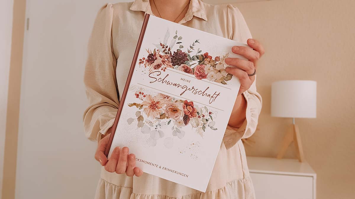 Frau hält ein schön gestaltetes Schwangerschaftstagebuch mit floraler Verzierung in den Händen.