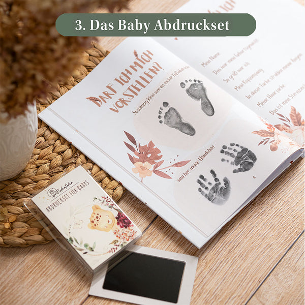 Eulentaler Baby-Abdruckset mit Stempelkissen sowie schwarzen Hand- und Fußabdrücken im geöffneten Babyalbum auf der Seite „Darf ich mich vorstellen?“.
