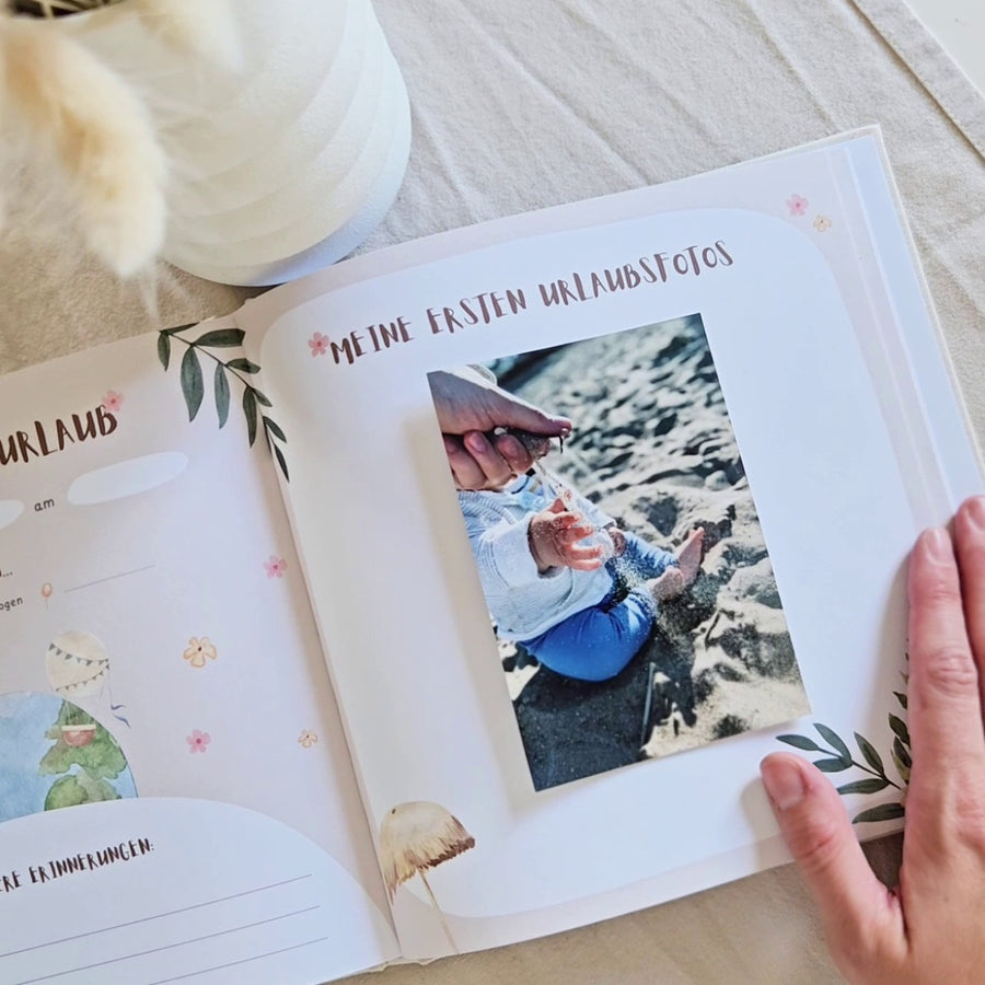 Geöffnetes Eulentaler Babyalbum mit der Seite „Meine ersten Urlaubsfotos“, eingeklebtem Babyfoto am Strand und Platz für persönliche Urlaubserinnerungen.
